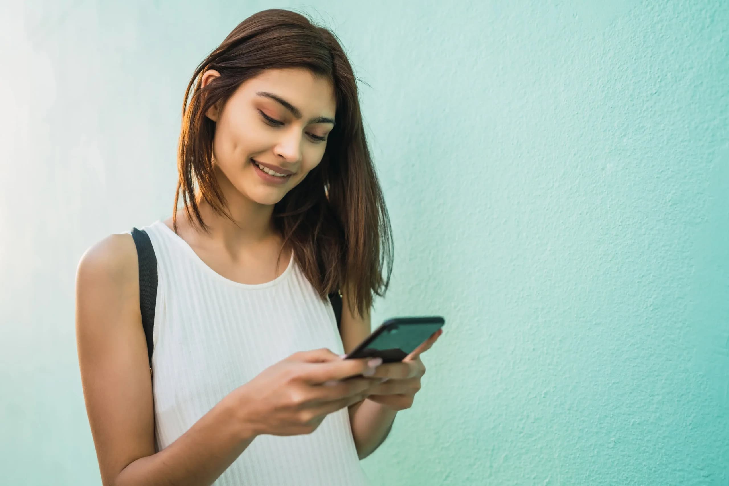 Smiling woman looking at her phone against a soft mint wall
